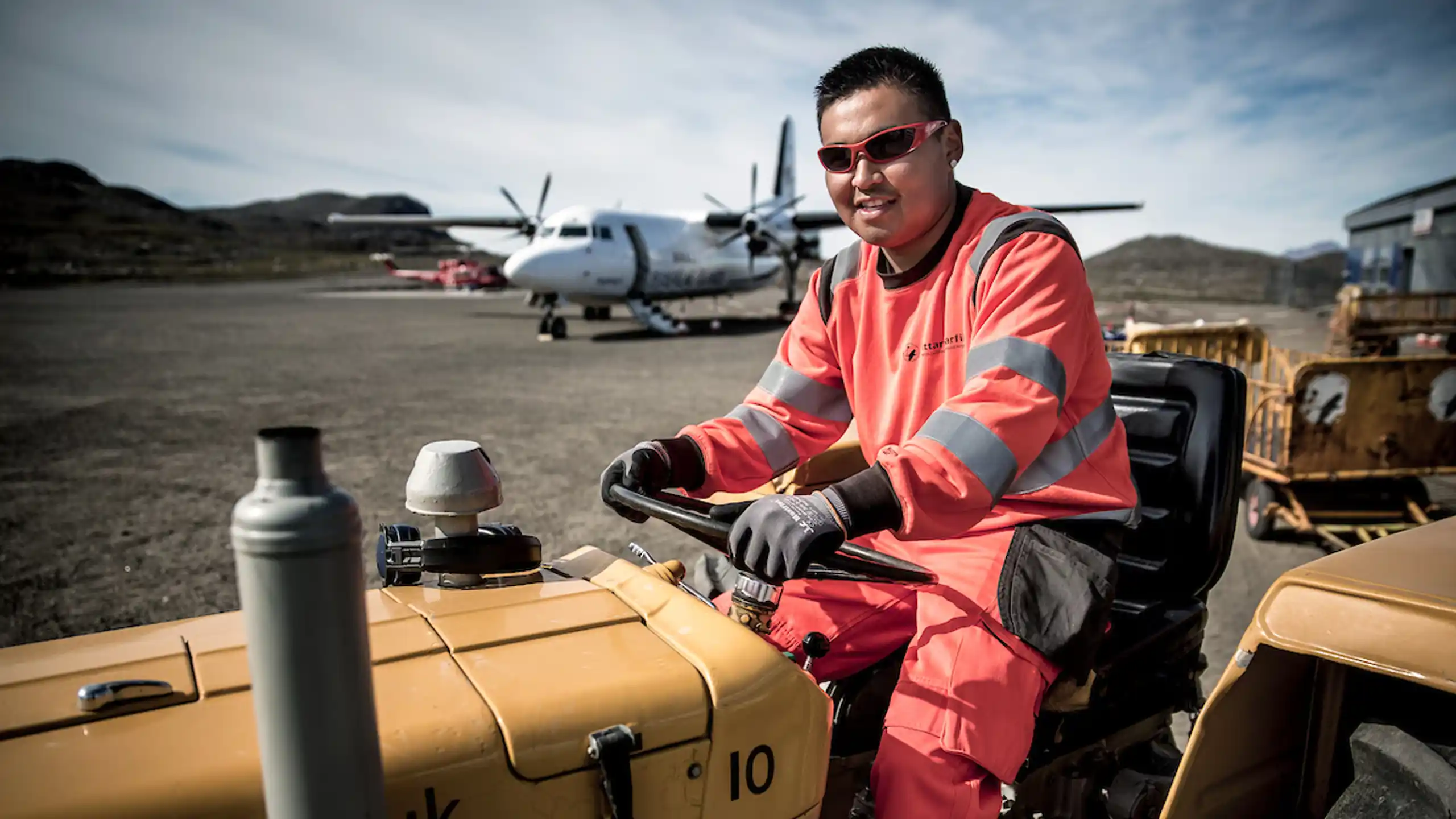 An Airport Worker At Kulusuk Airport In East Greenland With An Air Iceland Plane In The Background