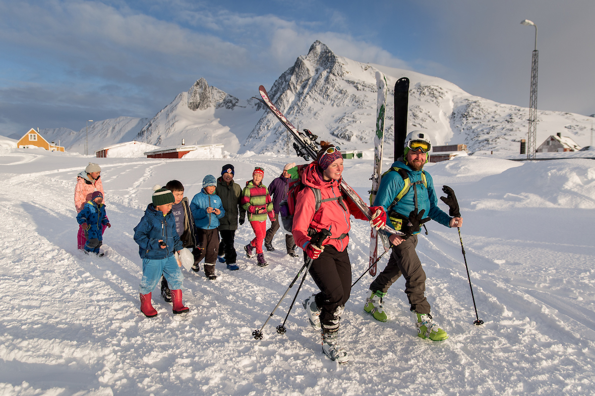 Skiers Walking Through Kuummiut In East Greenland With An Entourage Of Kids Behind Them
