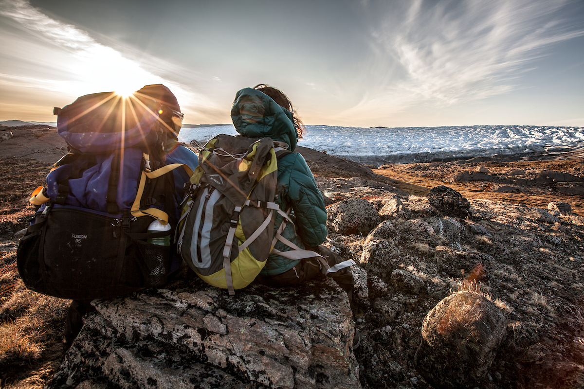 Two Hikers Enjoying The Sunset Over The Edge Of The Greenland Ice Sheet Near Kangerlussuaq
